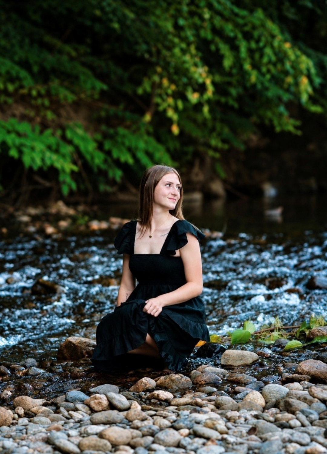 young woman kneeling on river rocks