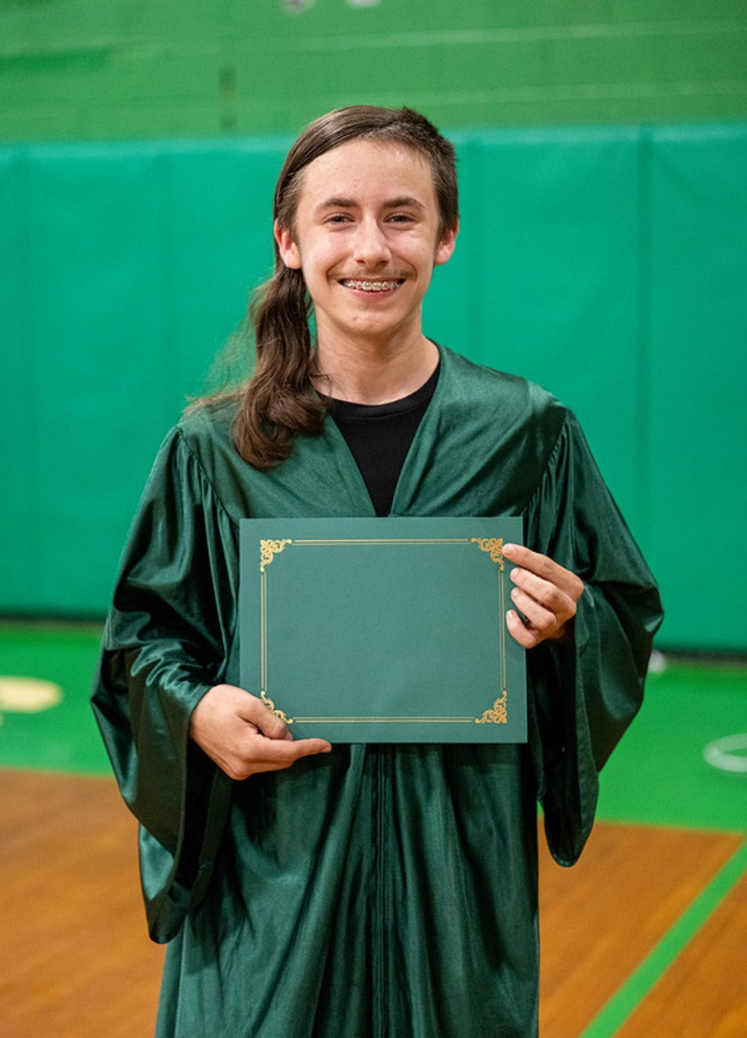 young man in green graduation gown holding green diploma