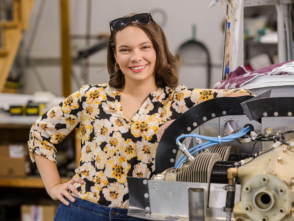 young woman in floral shirt smiling and leaning on an engine