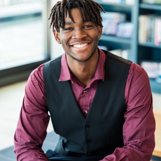 young man in burgundy shirt and black vest smiling