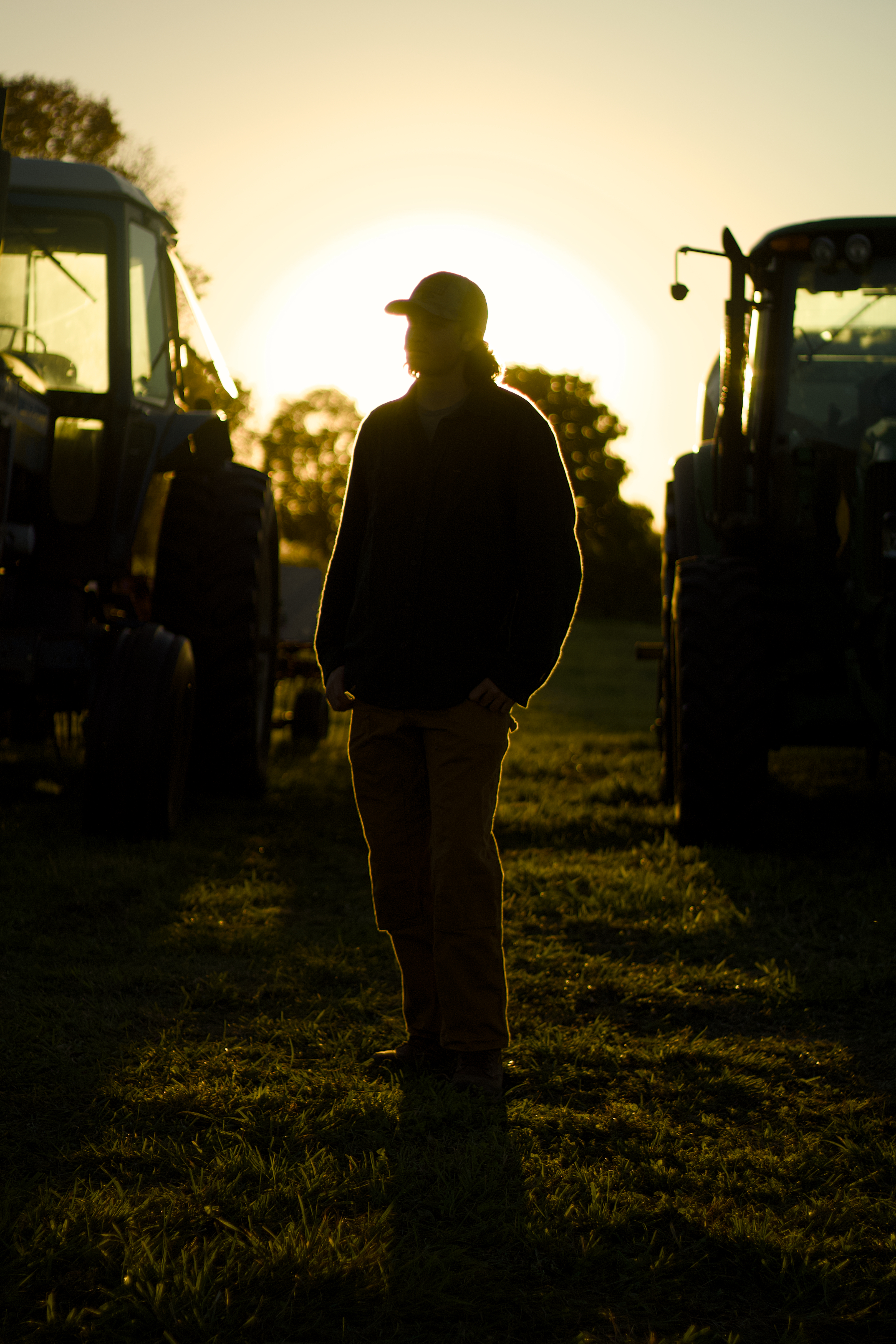 Young man standing between two tractors at sunset