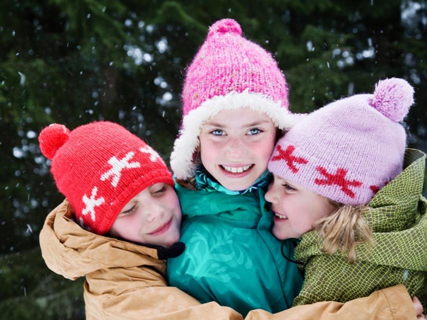 three kids hugging in front of evergreen trees