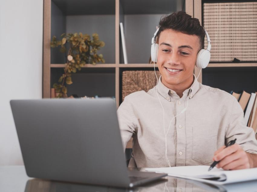 young male on laptop and writing on notepad