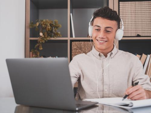 young male on laptop and writing on notepad